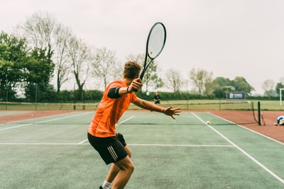 身穿橙色衬衫和黑色短裤、手持黑白网球拍的男子